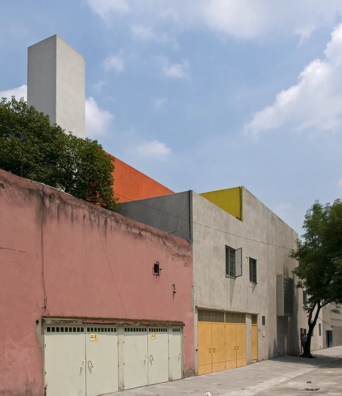 Front Casa Luis Barragán od strony ulicy, z różową ścianą, żółtymi i pomarańczowymi płaszczyznami oraz białą wieżą ciśnień powyżej
