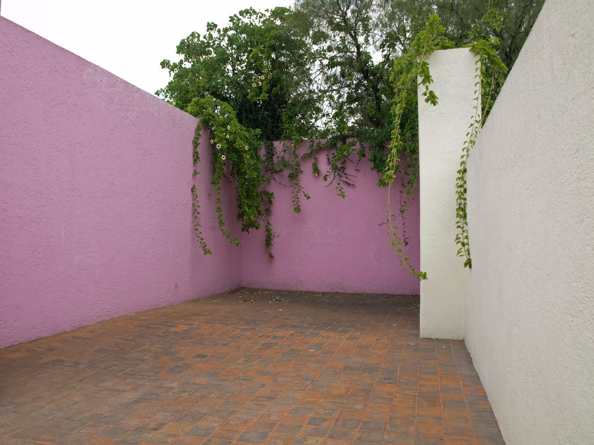 Η βεράντα στην ταράτσα της Casa Luis Barragán, περικλεισμένη από έναν ροζ και έναν λευκό τοίχο, με πράσινο να ξεχύνεται κάτω από τον ουρανό